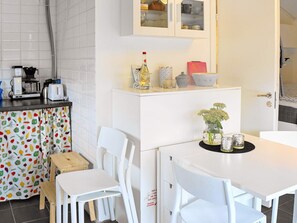 A compact kitchen with white cabinets, a coffee machine, and a toaster. There is a small dining area with a white table and chairs. - 4 Person Holiday Home in Skarhamn (Skaerhamn)