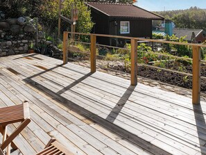 A wooden deck with a metal railing, a small wooden building, and a stone wall in the background. - 4 Person Holiday Home in Skarhamn (Skaerhamn)