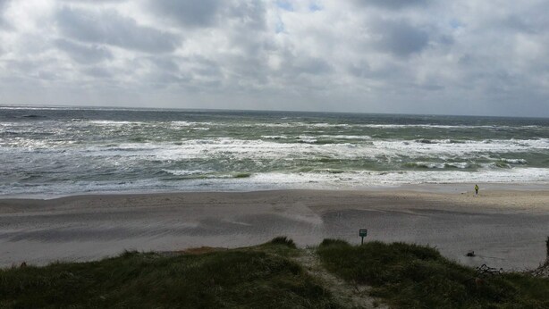 Une plage aux vagues agitées, sous un ciel nuageux.