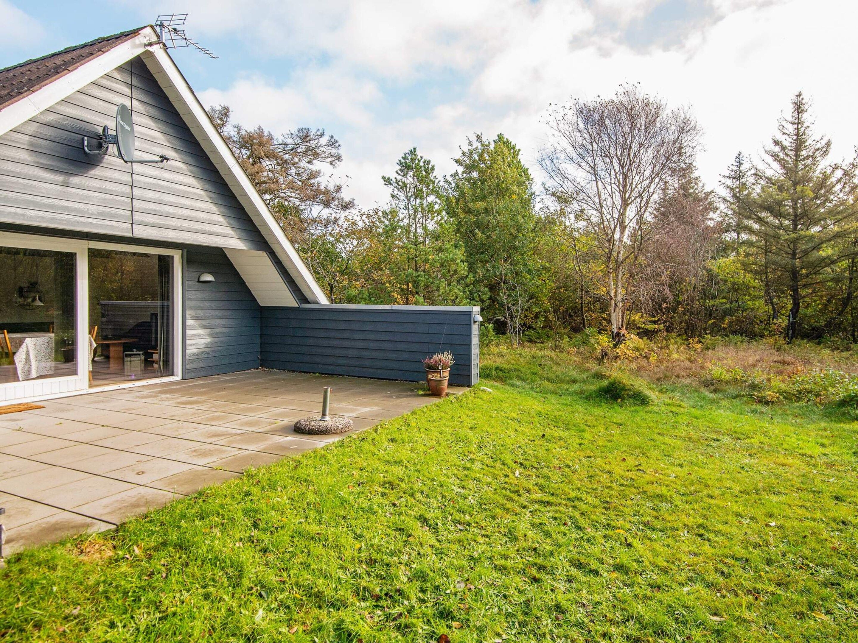 A modern house with a sloped roof, a patio with a table and chairs, and a garden with a potted plant.