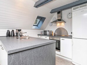 A modern kitchen with a central island, built-in oven, and a clock on the wall. - Tranquil Holiday Home in Ringkøbing near Sea (Ringkobing)