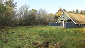 Une maison moderne avec un toit en pente, entourée d’un champ herbeux et d’arbres.