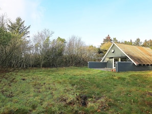 A modern house with a sloped roof, surrounded by a grassy field and trees. - Tranquil Holiday Home in Ringkøbing near Sea (Ringkobing)