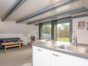 A modern kitchen with a large island, a dining area with a sofa and chairs, and a view of the outdoors. - Tranquil Holiday Home in Ringkøbing near Sea (Ringkobing)