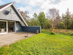 A modern house with a sloped roof, a patio with a table and chairs, and a garden with a small shed. - Tranquil Holiday Home in Ringkøbing near Sea (Ringkobing)