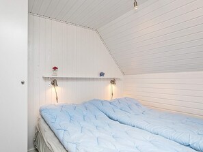 A bedroom with two beds, a sloped ceiling, and a shelf with a vase and a small item.