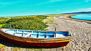 Un bote en una orilla pedregosa, con un lago y un bosque al fondo.