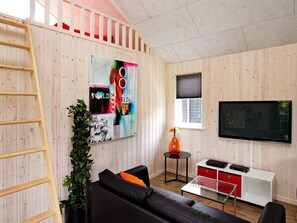 Una sala de estar moderna con un sofá de cuero negro, una mesa de centro de vidrio, un televisor montado en la pared y una escalera de madera apoyada contra la pared.
