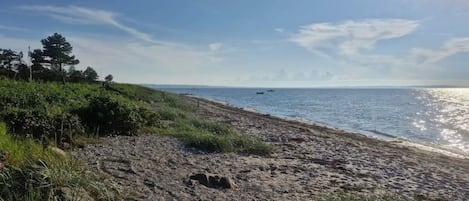 A beach with a clear sky, a rocky shoreline, and a few boats in the distance.