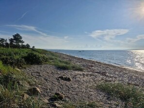 A beach with a clear sky, a rocky shoreline, and a few boats in the distance.