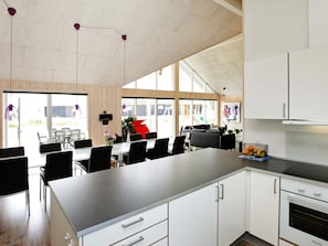 A modern kitchen with white cabinets, a built-in oven, and a dining area with a long table and chairs. - 4 Star Holiday Home in Bogense (Bogense)