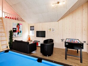 Una habitación con mesa de billar, sofá, televisión y mesa de futbolín.