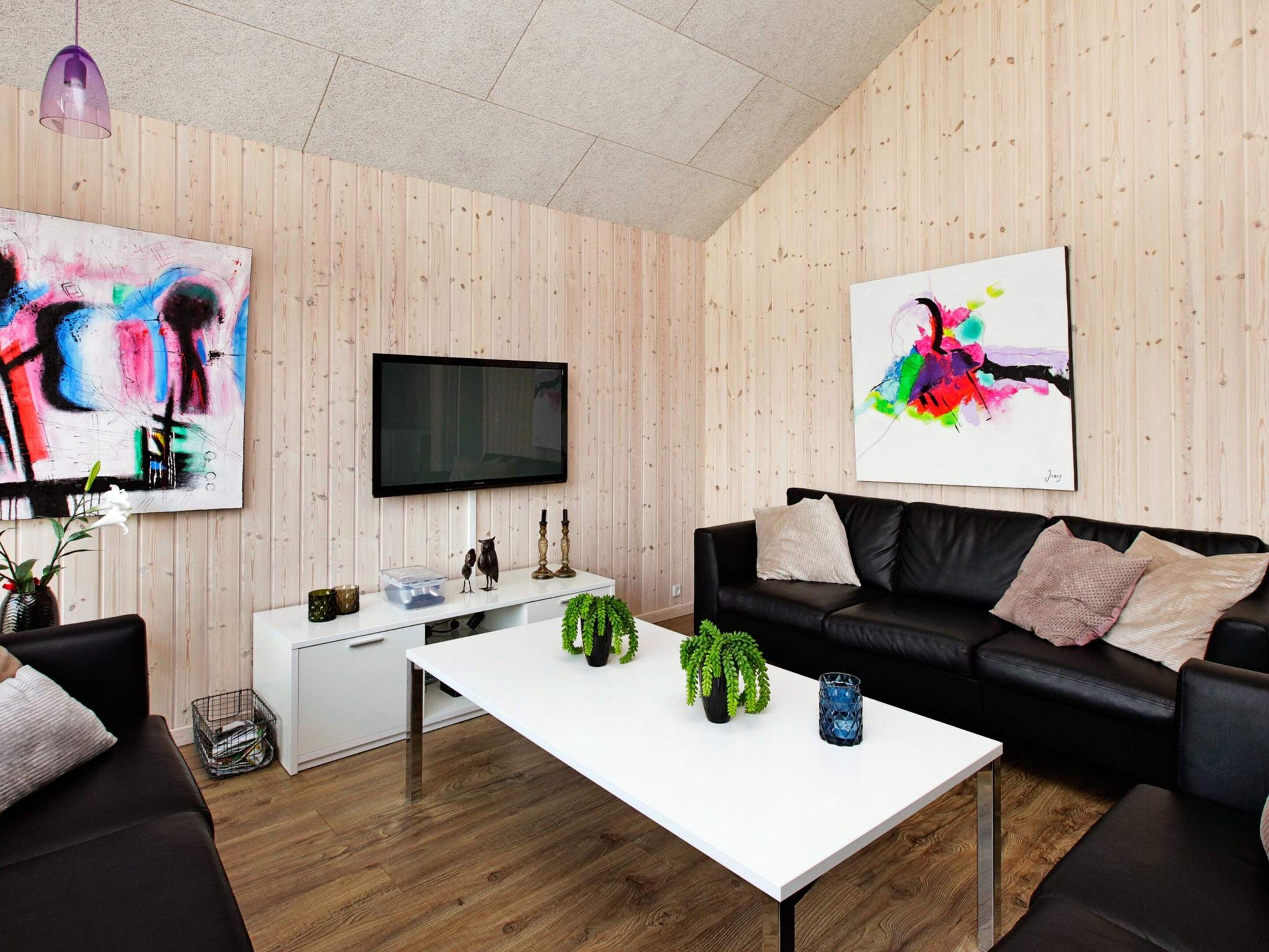 Ein modernes Wohnzimmer mit einem weißen Couchtisch, einer schwarzen Ledersofa und zwei abstrakten Gemälden.
