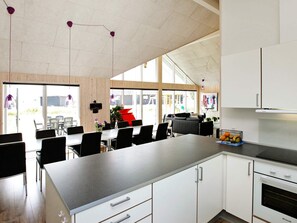 A modern kitchen with white cabinets, a built-in oven, and a dining area with black chairs and a white table. - 4 Star Holiday Home in Bogense (Bogense)