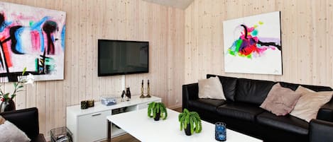 A modern living room with a white coffee table, black leather sofa, and two abstract paintings.