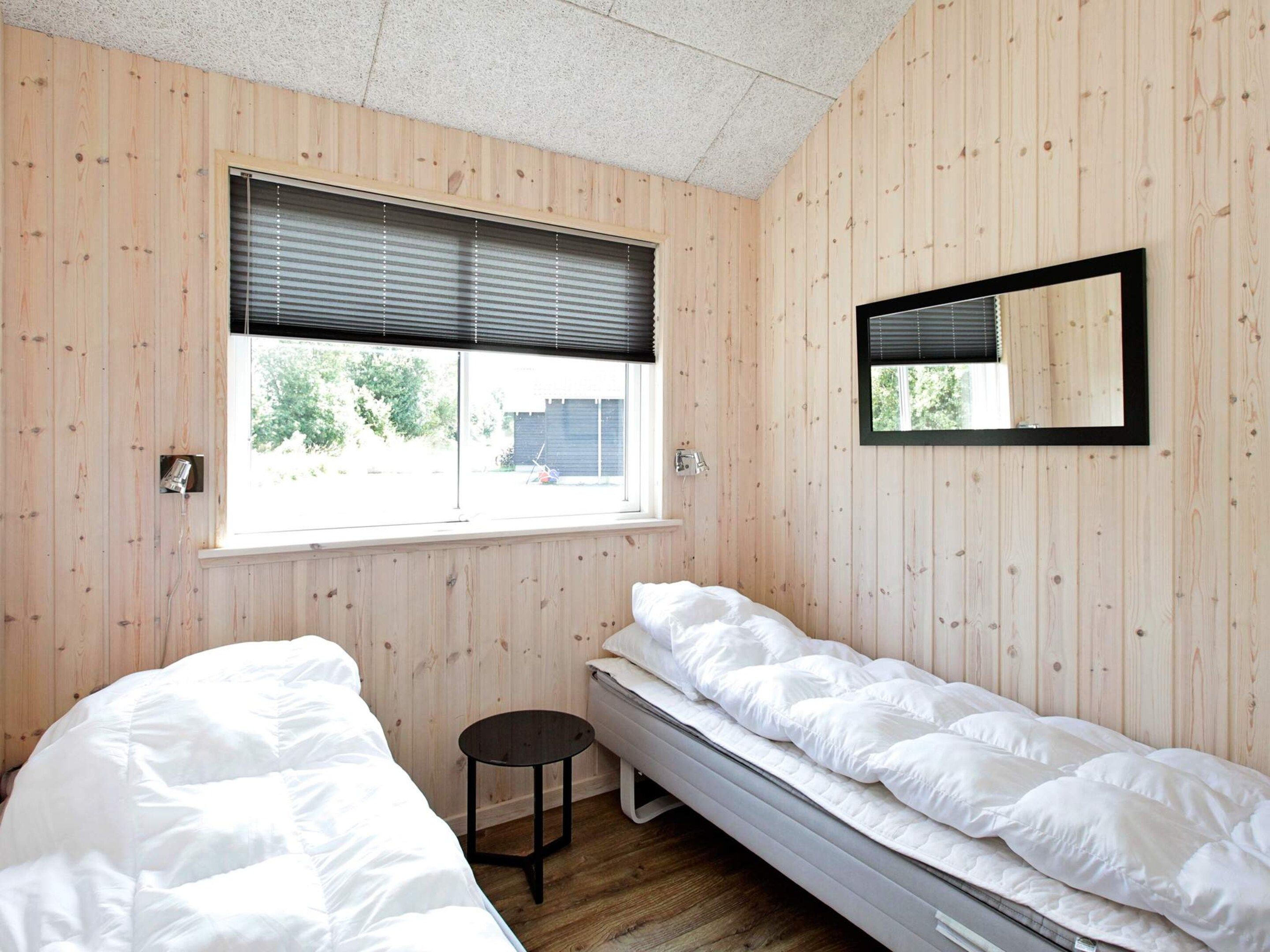 Una habitación con dos camas, una mesita, una ventana con persianas y un espejo en la pared.