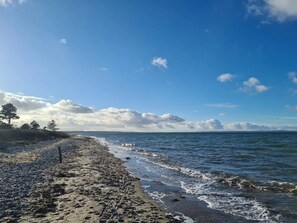 Una playa con costa rocosa, olas y un cielo despejado con nubes.