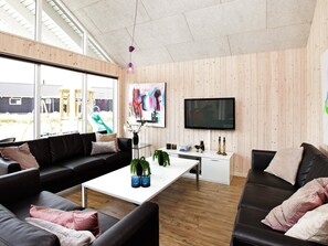A modern living room with a black leather sofa, a white coffee table, and a television mounted on the wall. - 4 Star Holiday Home in Bogense (Bogense)