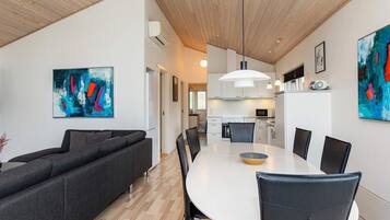 Una sala moderna con sofá, mesa de comedor y sillas. Cuenta con una zona de cocina con armarios y electrodomésticos.