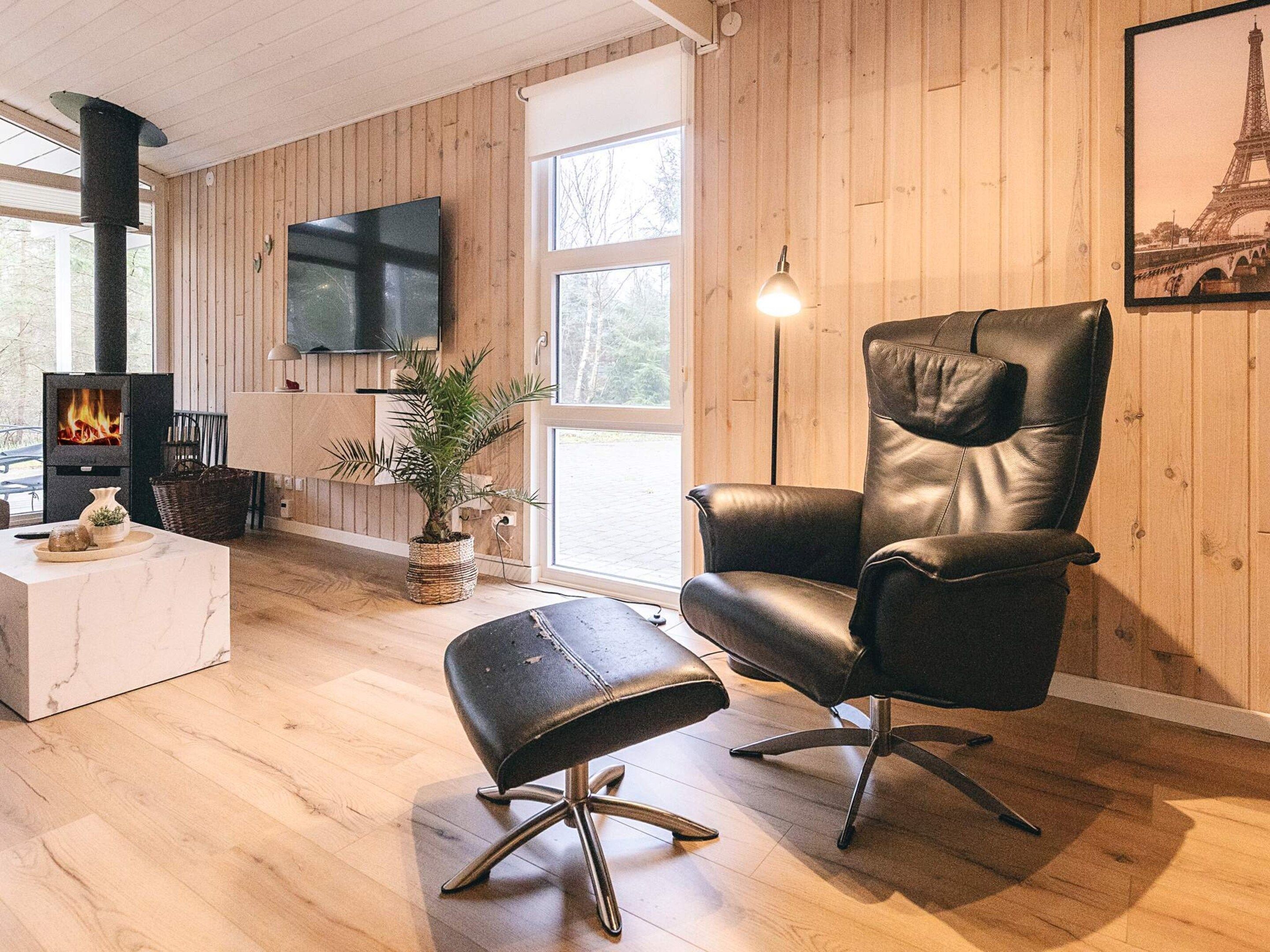 A living room with a black leather chair, a white marble coffee table, a wooden floor, a fireplace, and a TV mounted on the wall.