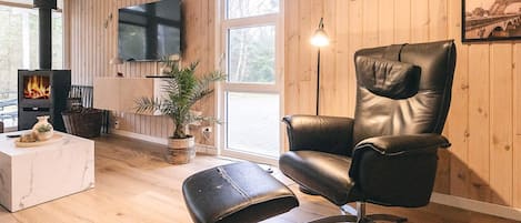 Een woonkamer met een zwarte leren fauteuil, een witte marmeren salontafel, een houten vloer, een open haard en een aan de muur bevestigde televisie.