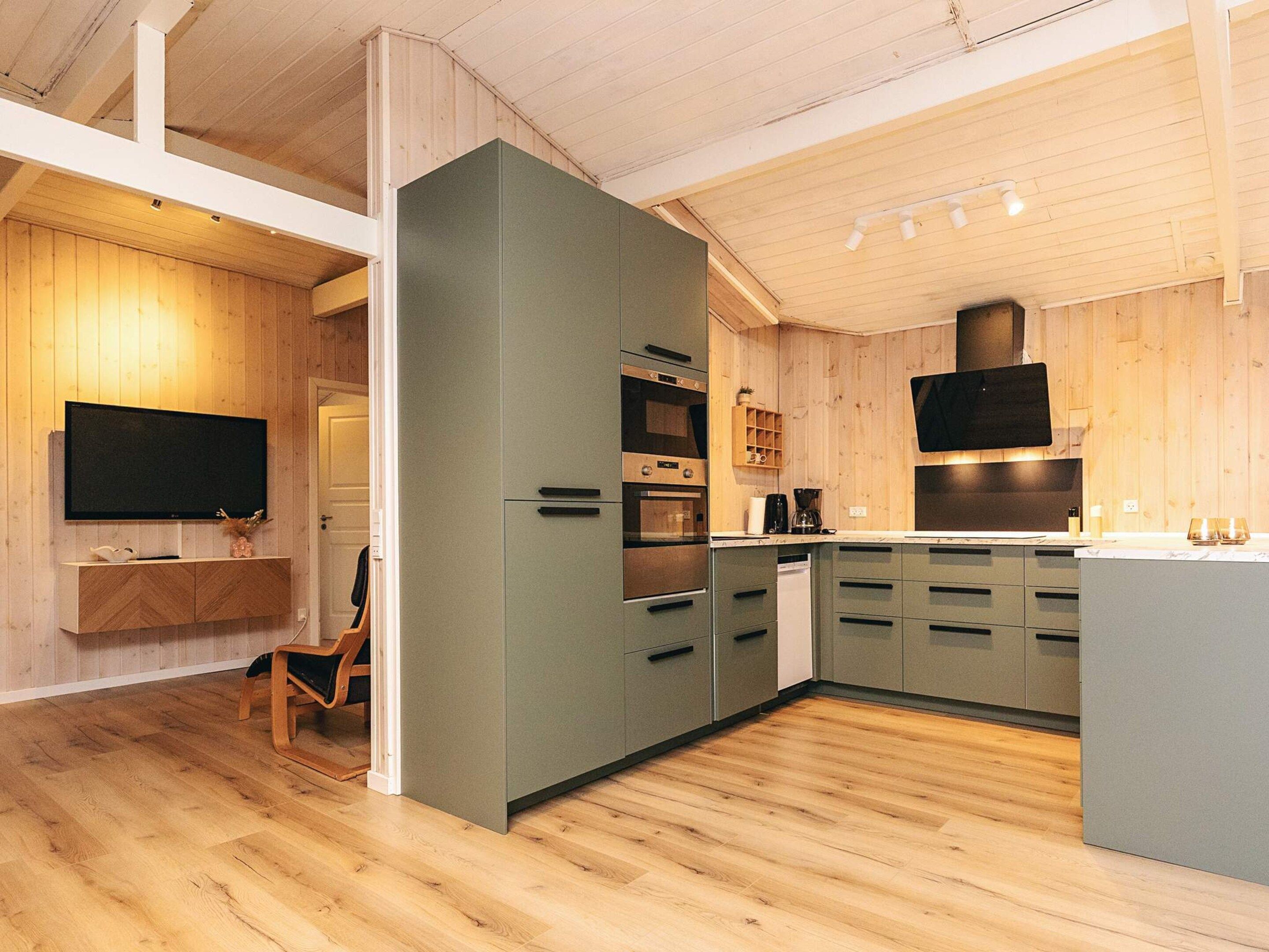 A modern kitchen with wooden flooring, built-in appliances, and a flat-screen TV.