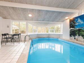 An indoor swimming pool with a view of trees through large windows, a poolside seating area, and a ceiling with recessed lighting. - 8 Person Holiday Home in Hadsund-by Traum (Hadsund)