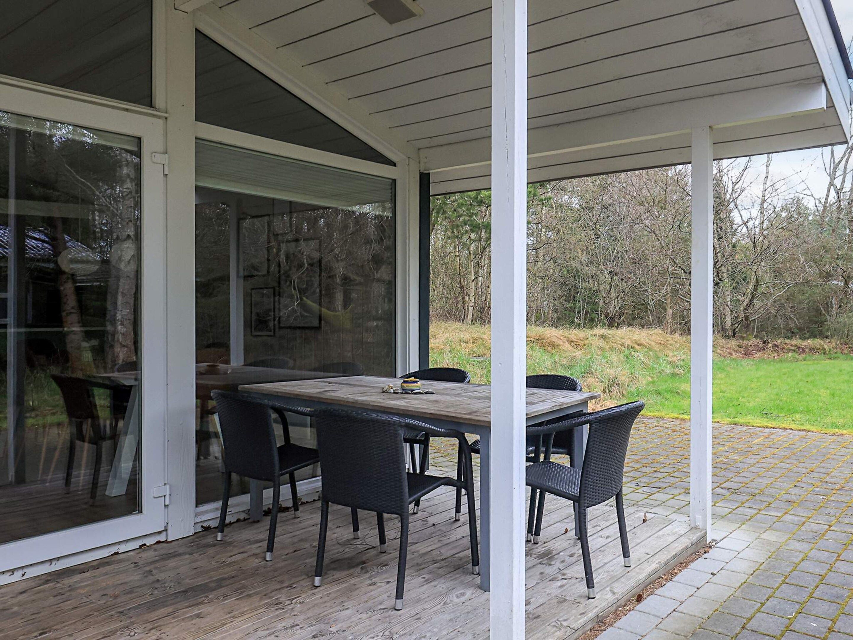 Un área de comedor al aire libre techada con una mesa, sillas, una puerta de vidrio y vista a un espacio con césped.