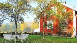 A red barn with white trim, surrounded by a grassy area with a table and chairs.