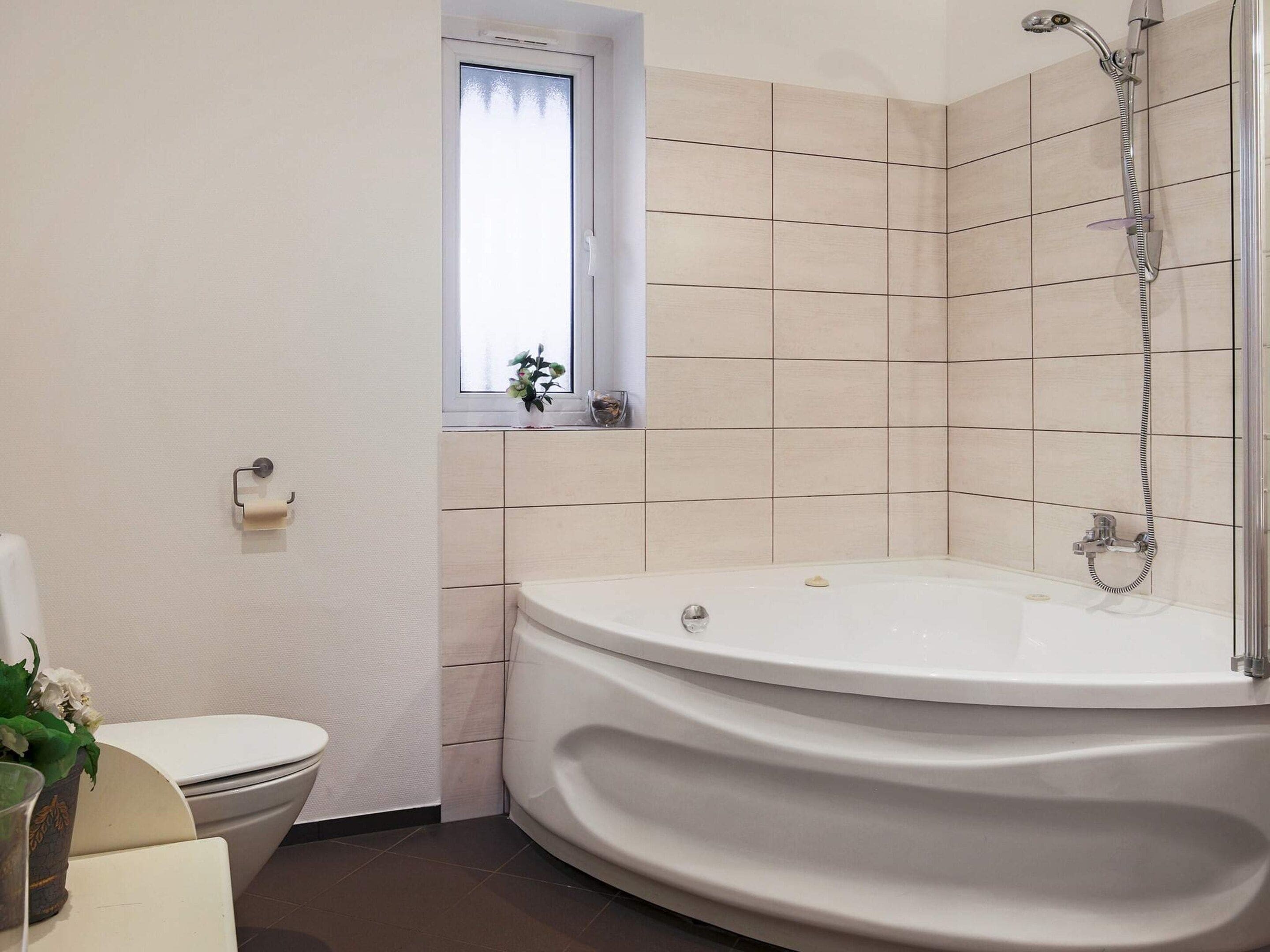 A bathroom with a bathtub, toilet, and a window.