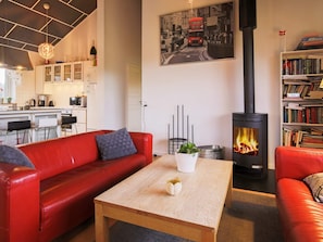 A living room with a red sofa, a wooden coffee table, a fireplace, a kitchen in the background, and a bookshelf. - 5 Star Holiday Home in Vaeggerlose (Vaeggerlose)