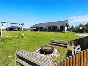 Une propriété résidentielle dotée d’une cour verdoyante, d’une balançoire, d’un foyer extérieur et d’une terrasse en bois.