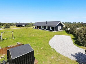 A residential property with a large grassy yard, a gravel driveway, and a black house with a sloped roof. - 5 Star Holiday Home in Vaeggerlose (Vaeggerlose)