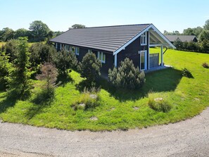 A single-story house with a dark roof and white trim, surrounded by a well-maintained lawn and trees. - 5 Star Holiday Home in Vaeggerlose (Vaeggerlose)