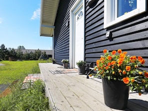 A house with a wooden deck, a potted plant with orange flowers, and a clear sky.