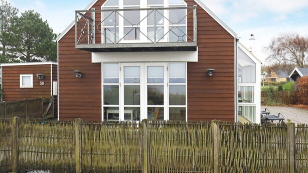 A two-story house with a balcony, large windows, and a wooden fence in front.