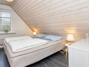 A bedroom with a sloped ceiling, a bed with white bedding, two bedside lamps, and a small table with a lamp. - 10 Person Holiday Home in Glesborg-by Traum (Glesborg)