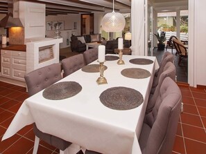 Un espace repas avec une longue table, des chaises à revêtement gris et un lustre.