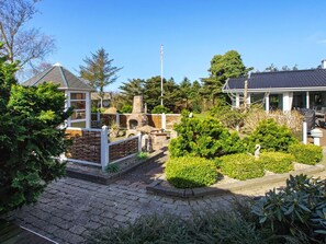 A residential area with a stone patio, a stone fireplace, and a well-maintained garden with various shrubs and a bird sculpture. - 5 Star Holiday Home in Hemmet (Hemmet)