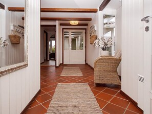A hallway with a woven chair, a mirror, and a door.