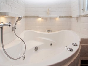 A white bathtub with a shower head, a control panel, and a drain.
