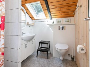 Ein kleines Badezimmer mit Oberlicht, weißen Fliesen, einem Waschbecken, einer Toilette und einem kleinen Hocker.