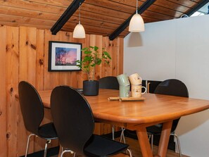A wooden dining table with four chairs, a potted plant, and a stack of mugs.
