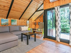 Et hyggeligt interiør i en hytte med træloft, sofa, bord og stol.