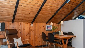 A cozy room with wooden walls and ceiling, a dining table with chairs, a sofa, and a small table with a plant and mugs. - 4 Person Holiday Home in Oksbol (Oksbol)