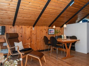 A cozy room with wooden walls and ceiling, a dining table with chairs, a sofa, and a small table with a plant and mugs. - 4 Person Holiday Home in Oksbol (Oksbol)
