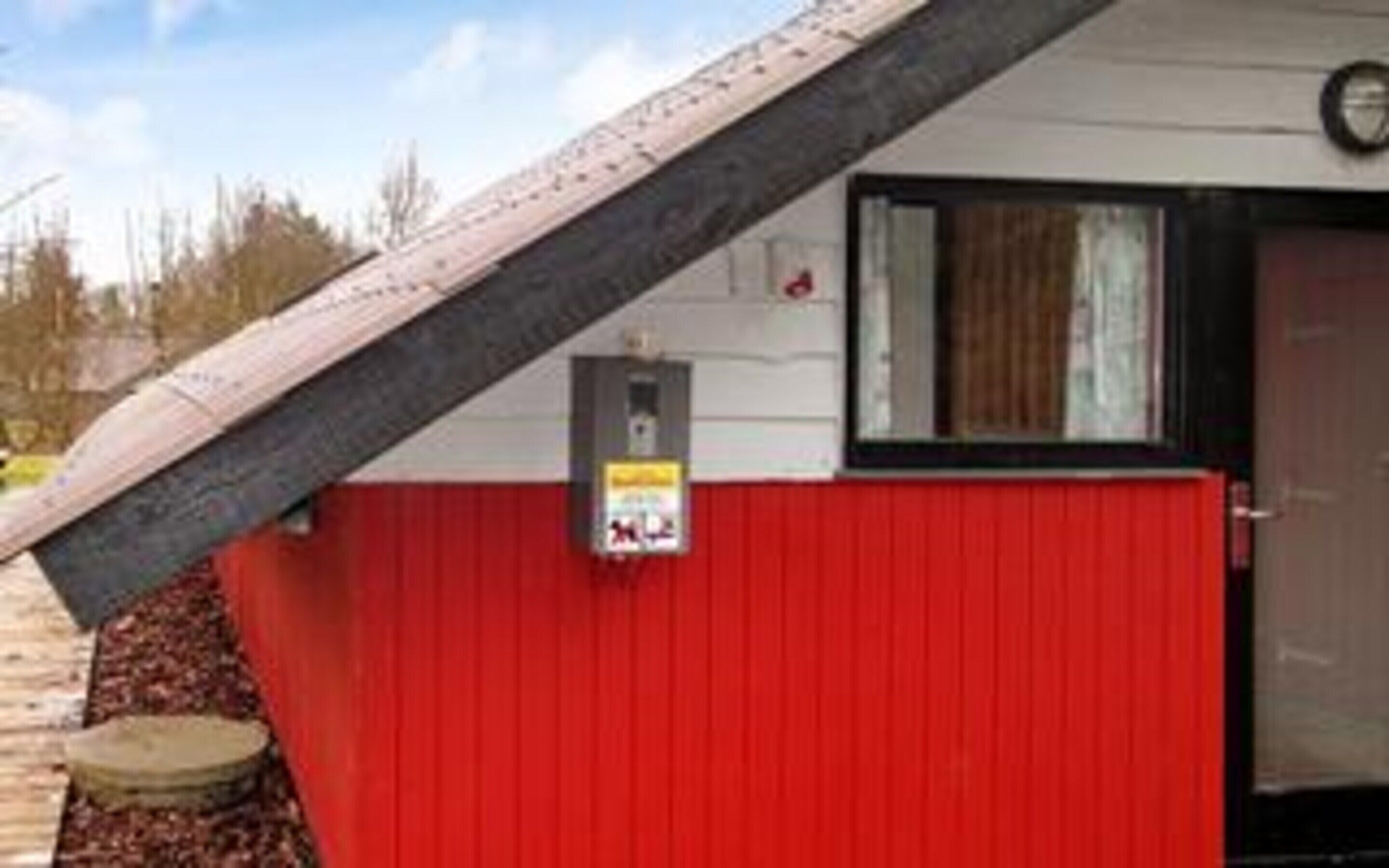 Un bâtiment à l’extérieur rouge, avec une porte noire et une petite fenêtre.