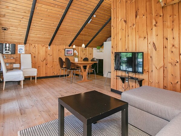 Ein gemütliches Zimmer mit Holzbalkendecke, einem Essbereich mit Tisch und Stühlen, einem Sofa und einem an der Wand befestigten Fernseher.