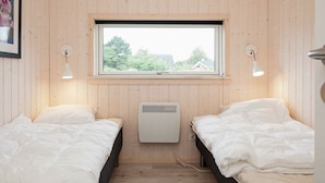 A room with two beds, a window with a view of greenery, and a wall-mounted heater.