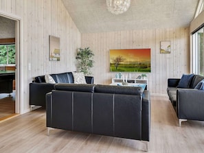 A modern living room with a wooden paneled wall, a large painting, and two black leather sofas.